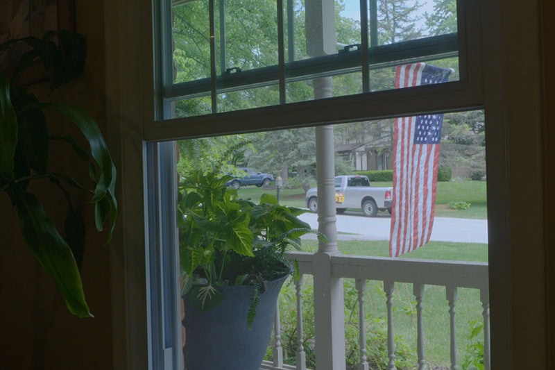 A window with a view of the front yard with an American flag hanging.